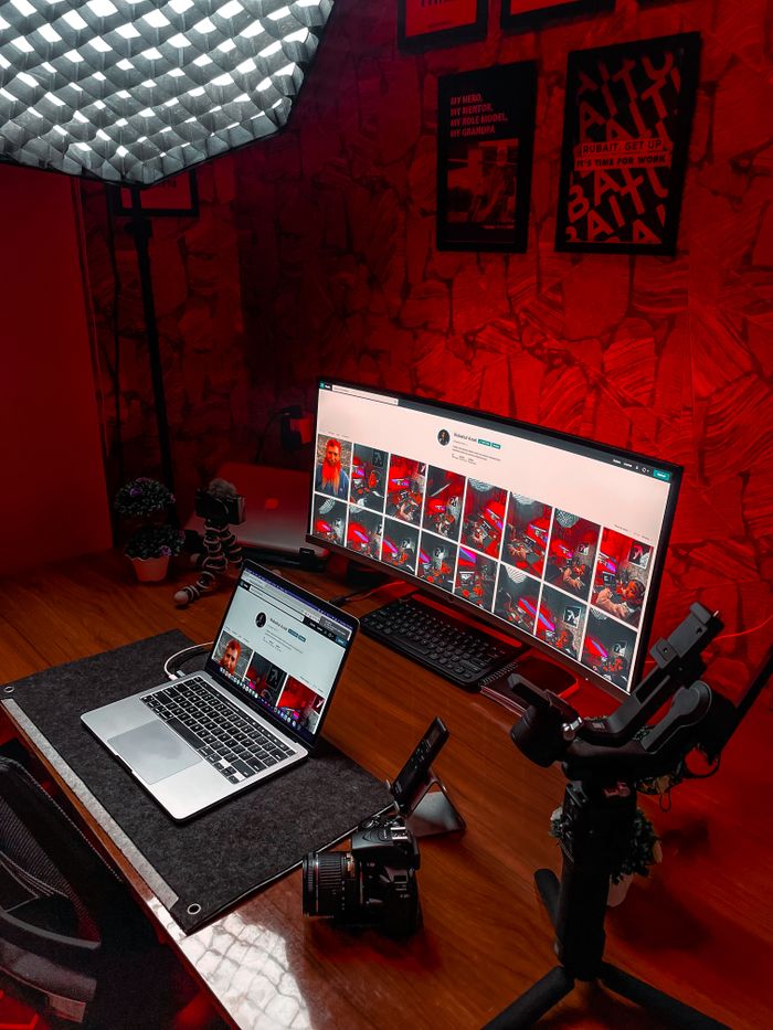 Stylish video editing setup featuring laptop and ultrawide monitor with striking red lighting.